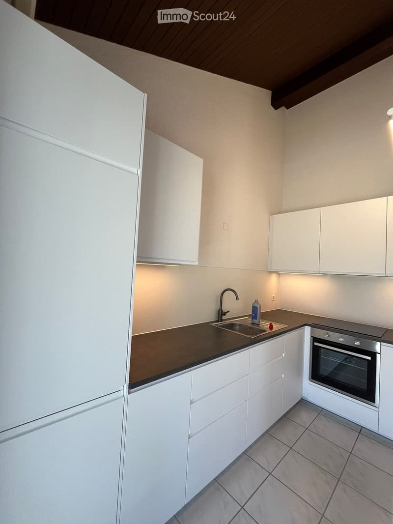 Modern kitchen with white cabinets, dark countertops, stainless steel sink, and oven. Features a bottle on the counter and a faucet above the sink.