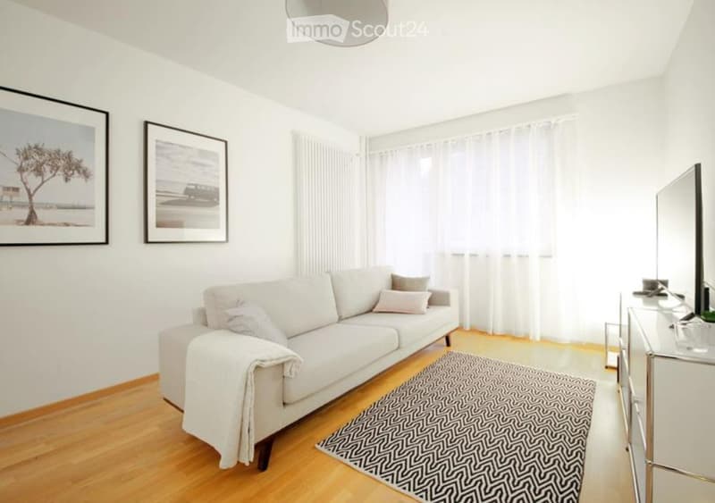 Modern living room with a white sofa, throw blanket, coffee table, mirror, and picture frames on the wall.