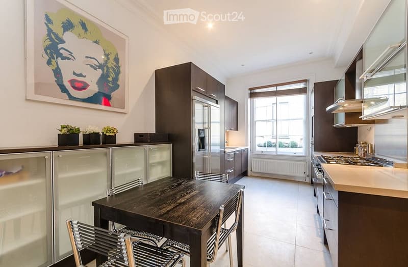 Modern kitchen with stainless steel appliances, dark wood dining table, and contemporary decor including a pop art painting and small flower pots.