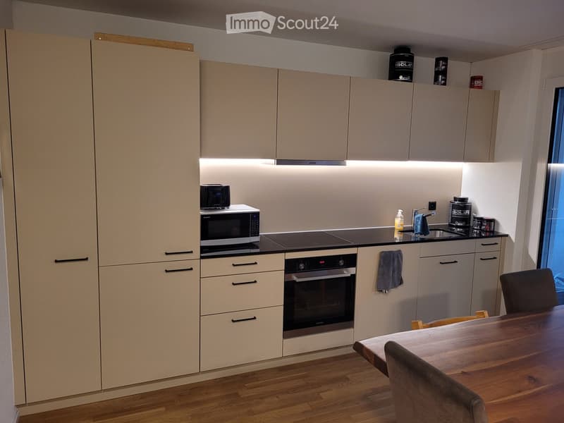 Modern kitchen with light-colored cabinets, a microwave, an oven, a wooden dining table, and a chair.