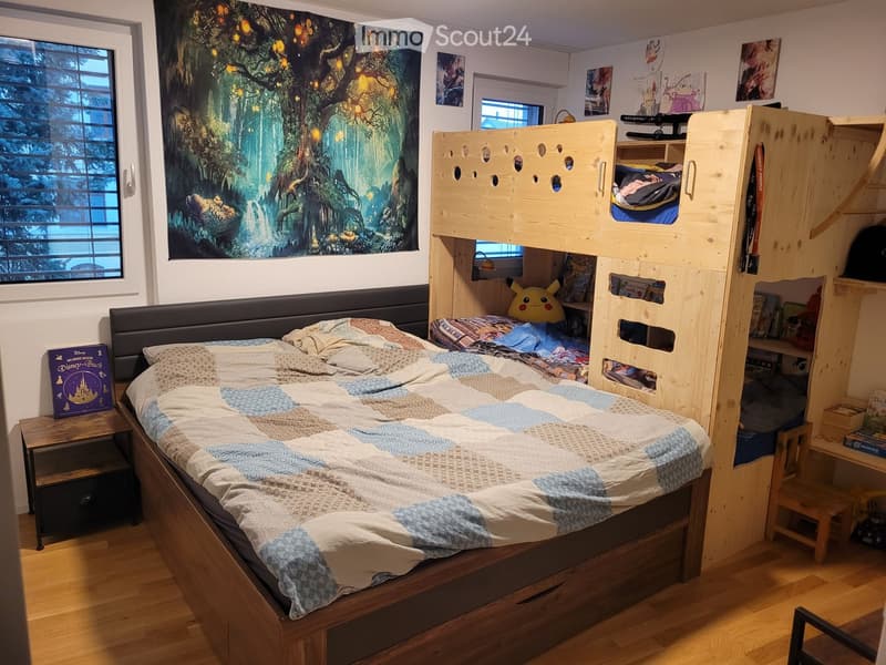 Cozy bedroom with a large bed, bunk bed, nightstand, bookshelf, and decorative artwork.