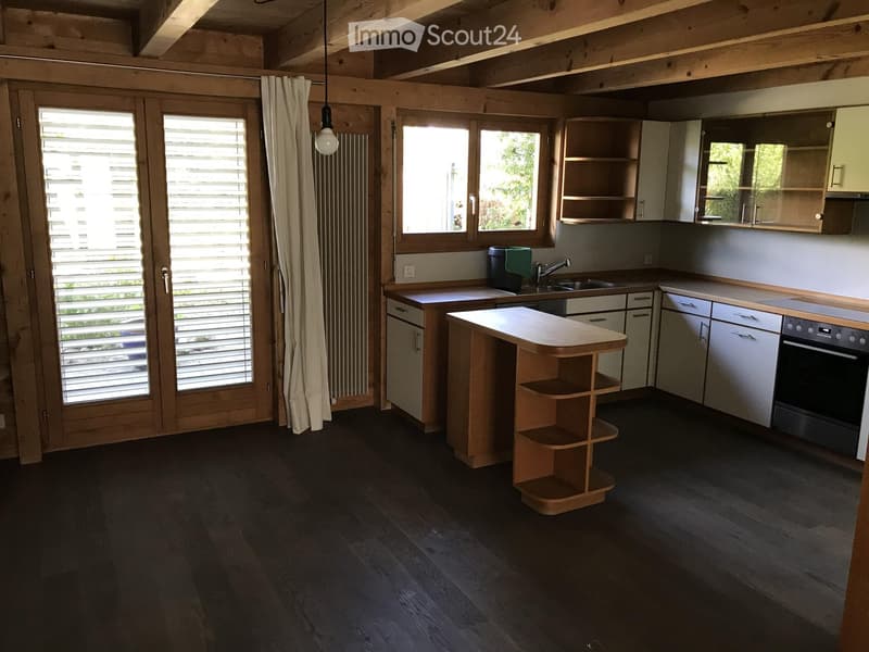 Modern kitchen with light wood cabinets, stainless steel appliances, island, and dark wooden flooring.
