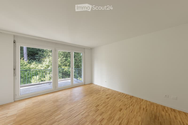 Empty room with wooden flooring, white walls, and large sliding glass doors leading to a balcony with a metal railing.