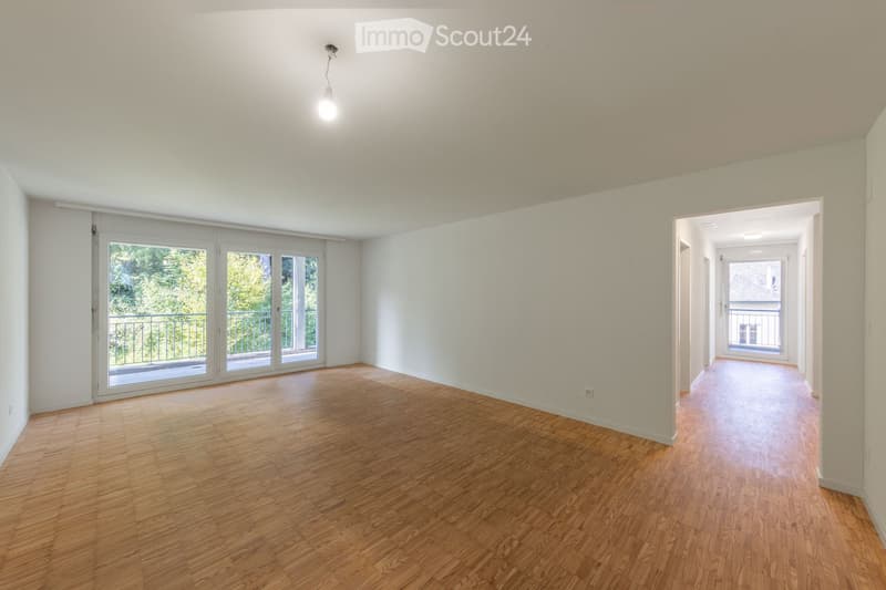 Empty room with wooden flooring, white walls, and large sliding glass doors leading to a balcony.