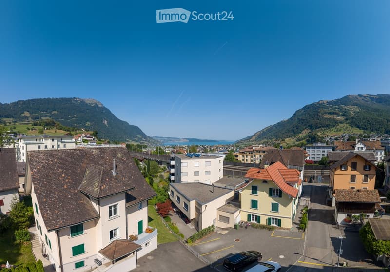 Aerial view of a residential area with multiple buildings, parking lot, and surrounding mountains and water body.