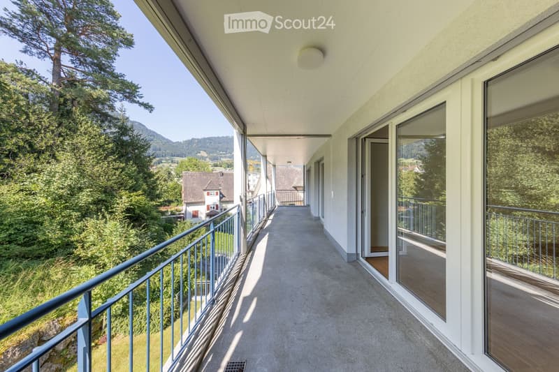 Balcony with a view of a green landscape and trees, featuring a metal railing and large windows.