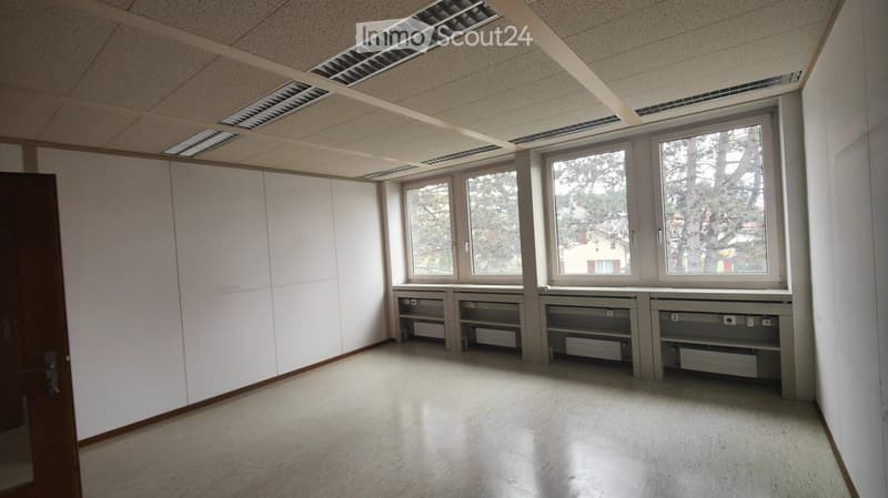 Empty room with white walls, large windows, built-in shelving units, and a door. No furniture or personal items are present.