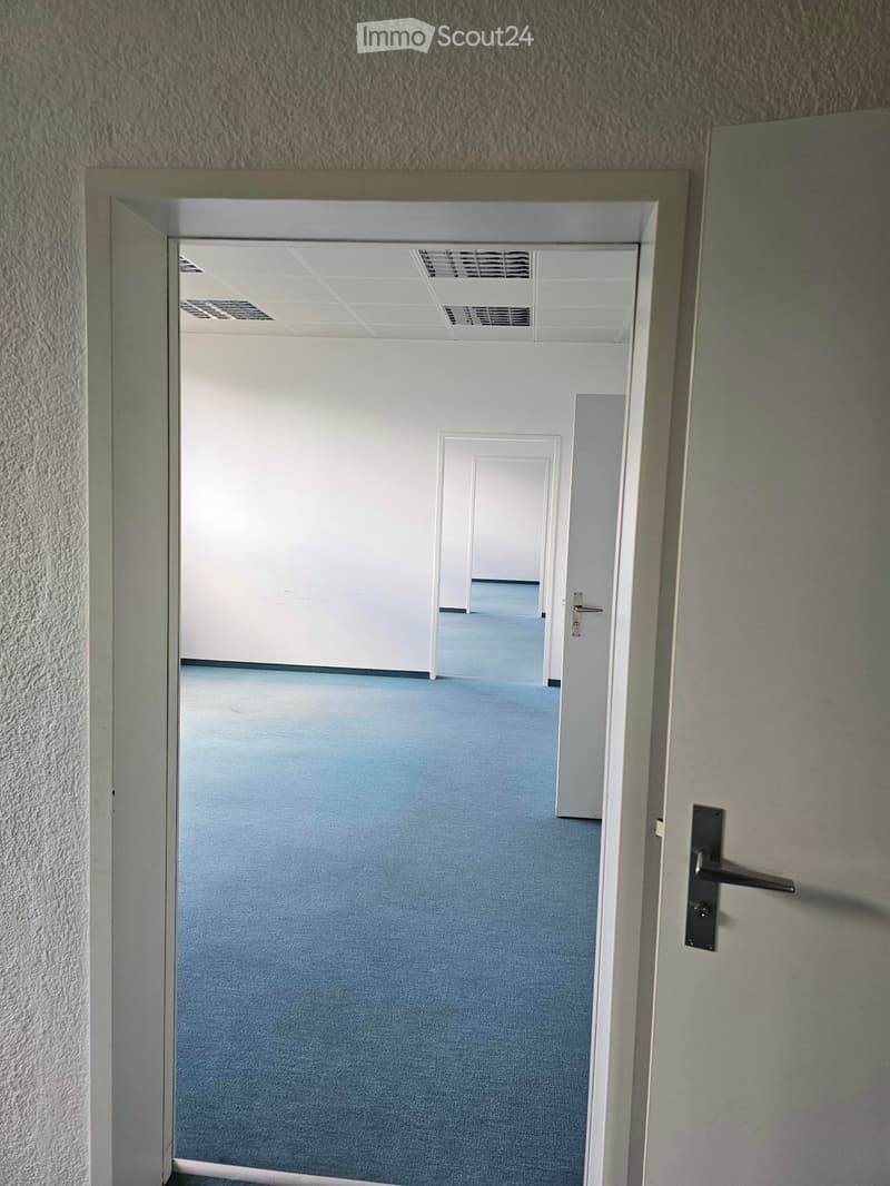 Empty hallway with light blue walls and white ceiling, featuring a closed door with a silver handle and a partially open door leading to another room.