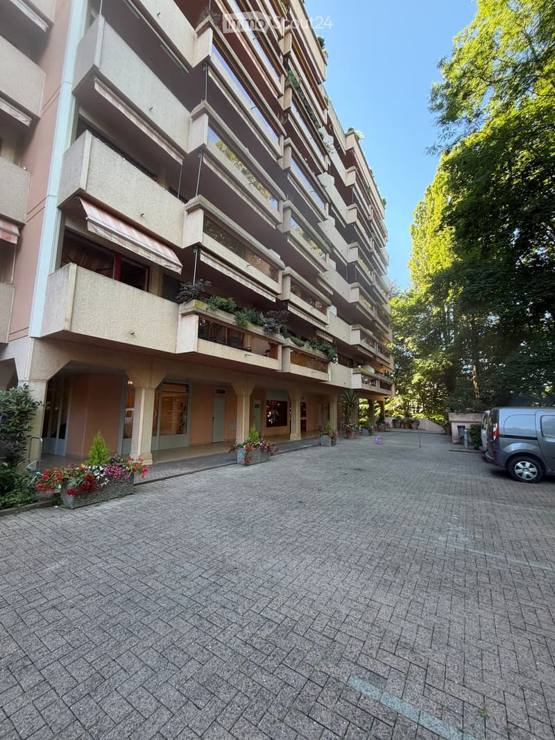 Multi-story residential building with balconies, potted plants, and a paved courtyard.