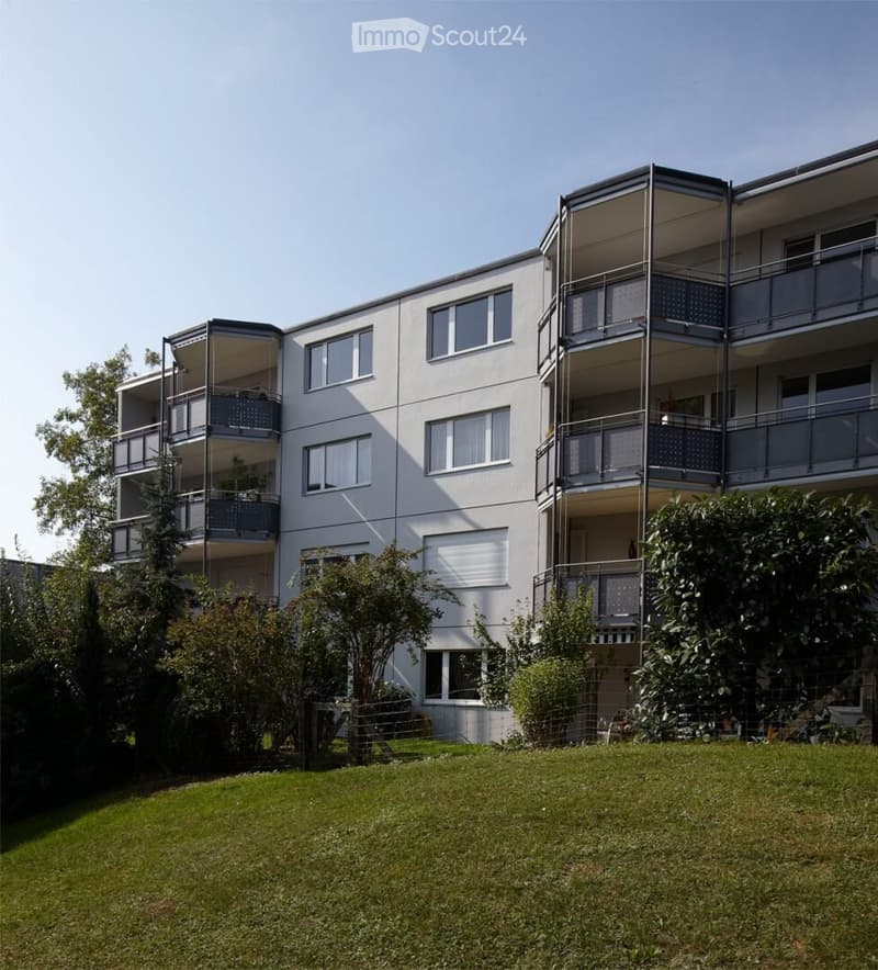 Modern multi-story apartment building with balconies, large windows, and surrounding greenery.