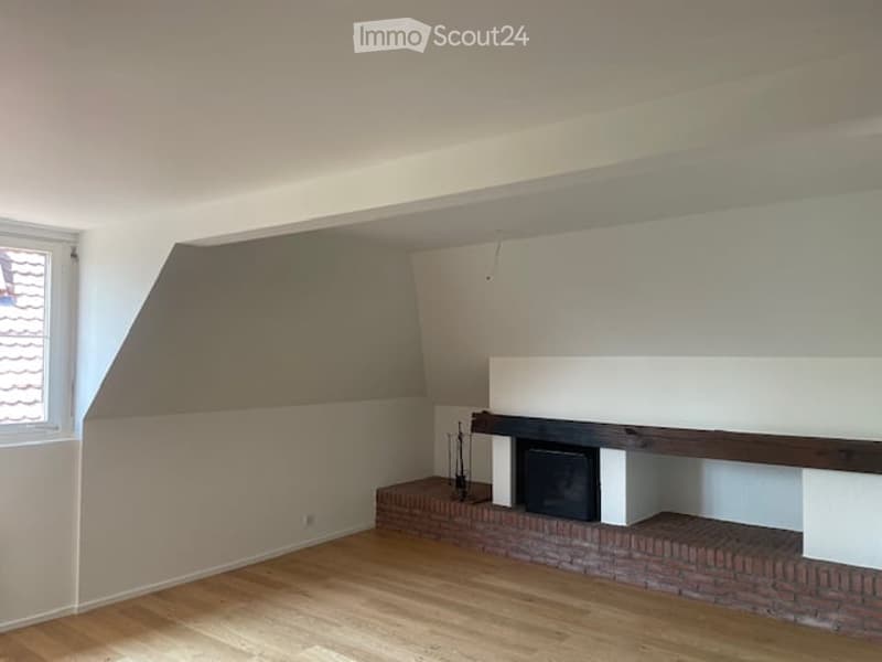Empty room with wooden flooring, white walls, and a fireplace with a brick surround.