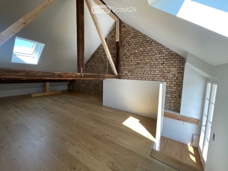 Empty attic space with exposed wooden beams, brick wall, skylight window, and wooden flooring.