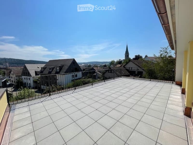 Spacious balcony with tiled floor, metal railing, and scenic view of the town and surrounding landscape.
