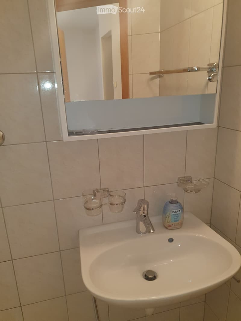 Bathroom with a white sink, chrome faucet, mirror cabinet, two glass cups, and a bottle of soap on the sink counter.