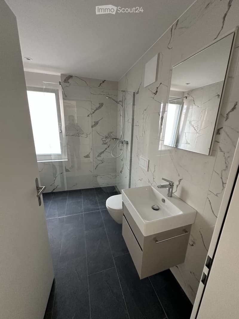 Modern bathroom with dark tiled floor, white marble walls, a sink with a modern faucet, a toilet, and a glass-enclosed shower area.