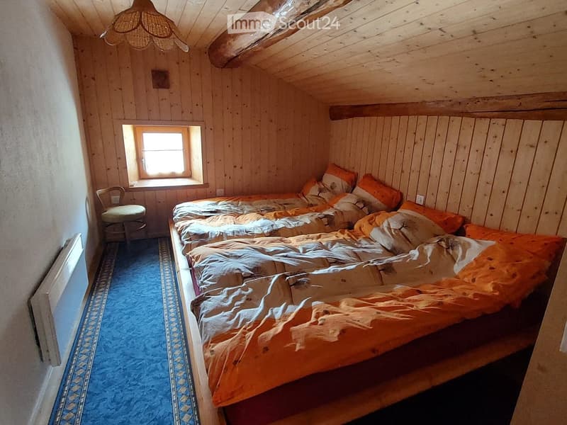 Cozy wooden bedroom with two single beds, orange bedding, a small chair, and a radiator near the window.