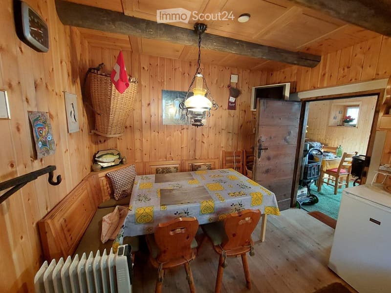 Cozy wooden-paneled room with a dining table, chairs, a refrigerator, and a radiator. A wicker basket and a mirror are on the wall.