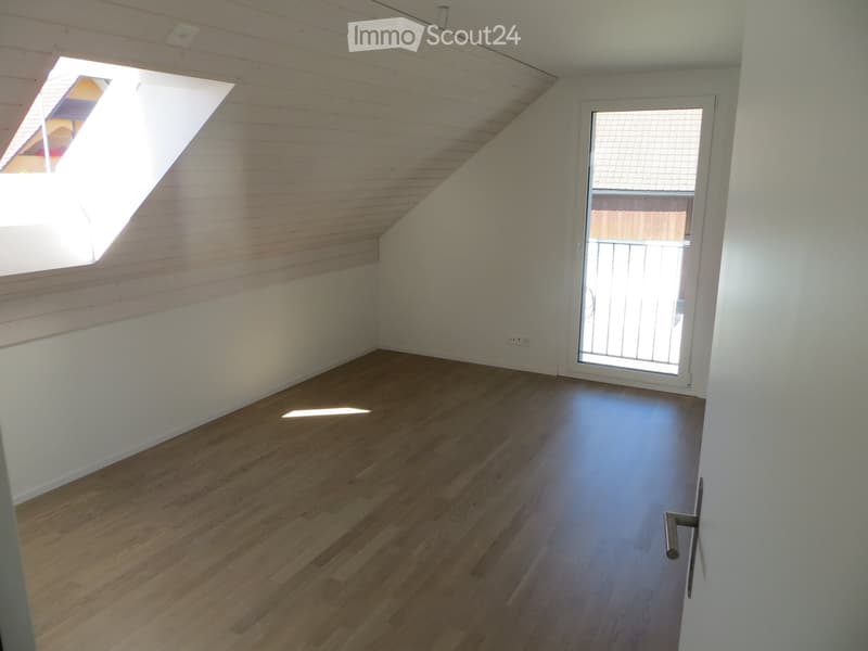 Empty attic room with wooden flooring, white walls, and a skylight window. The room features a sliding glass door leading to a balcony area.