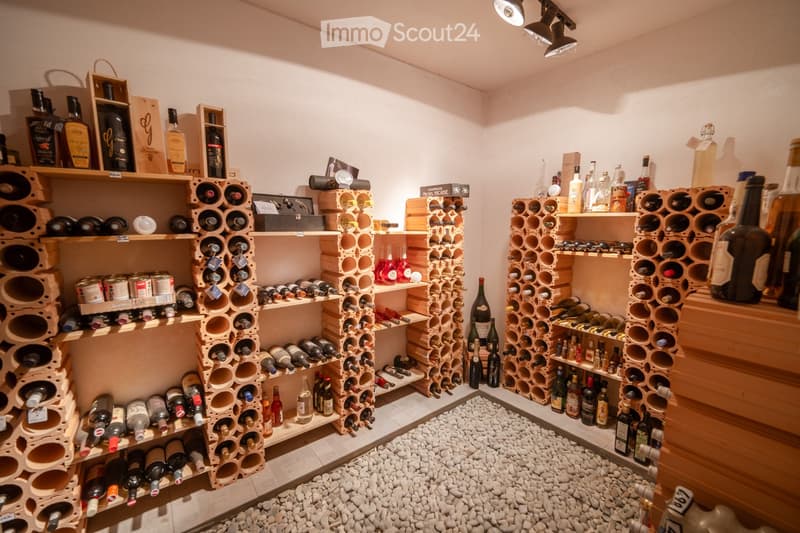 A well-organized wine cellar with multiple wooden racks filled with various wine bottles, shelves holding additional bottles and accessories, and a small clock on top.