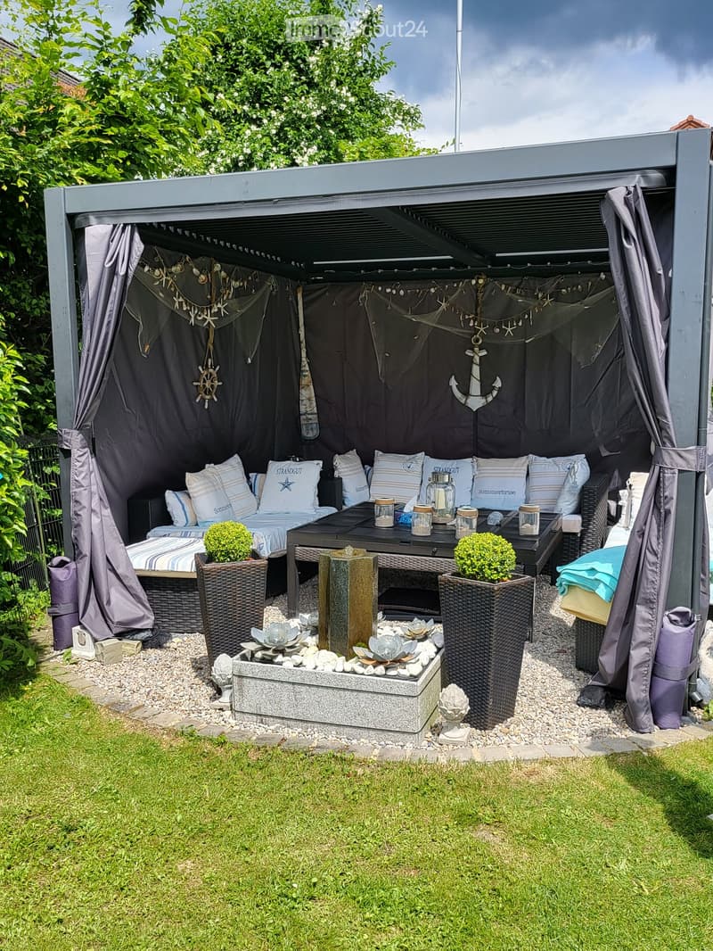 A cozy outdoor seating area with a sofa, table, and decorative elements, including potted plants and a small fireplace.