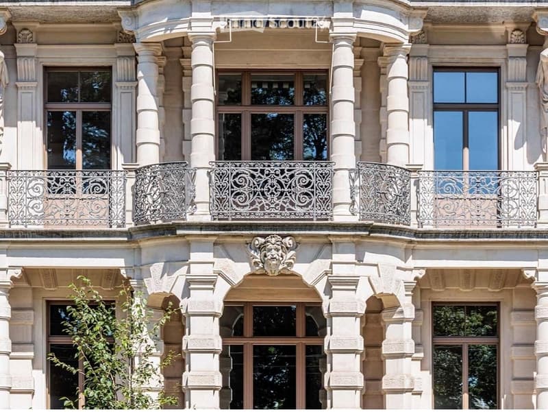 Ornate building facade with large windows, decorative columns, and wrought-iron balconies.