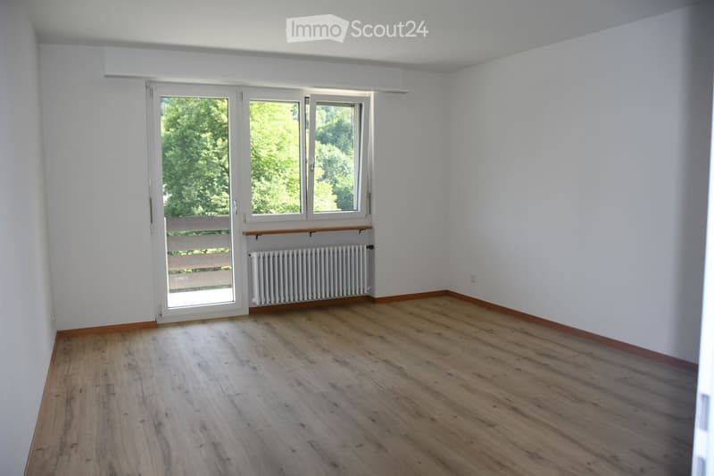 Empty room with wooden flooring, white walls, large windows, and a radiator. No furniture or equipment present.