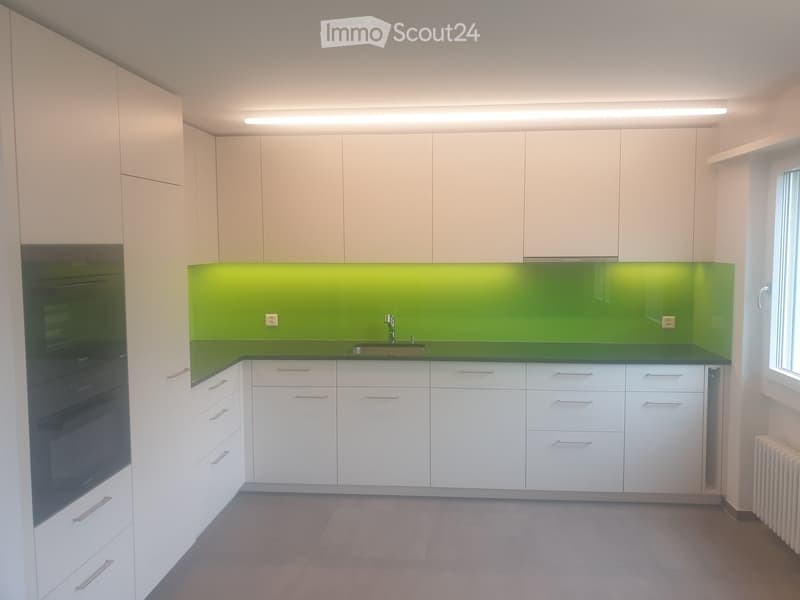 Modern kitchen with white cabinets, green backsplash, and stainless steel sink and faucet.