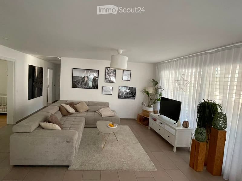 Modern living room with a large sectional sofa, coffee table, TV stand, side table, potted plants, and artwork on the walls.