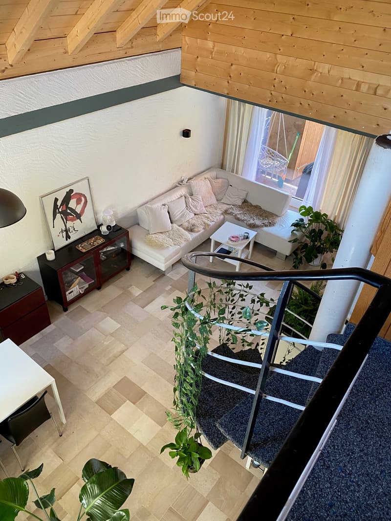 Modern living room with a white sofa, coffee table, small table, cabinet, and plants. The room features wooden beams on the ceiling and a staircase leading to another level.