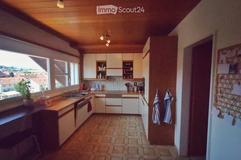 Bright kitchen with white cabinets, wooden countertops, and a tiled floor. Features a sink, dishwasher, and various kitchen appliances. A window offers a view of the surrounding area.