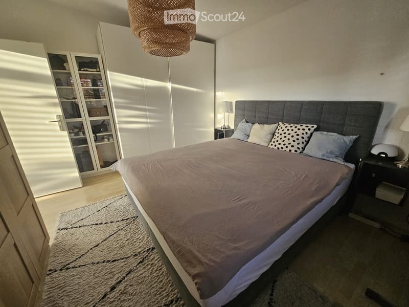 Modern bedroom with a large bed, nightstands, a wardrobe, and a hanging woven lamp.