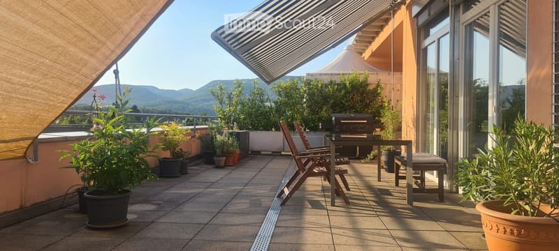 Balcony with tiled floor, outdoor furniture including a table and chairs, potted plants, and a view of mountains.