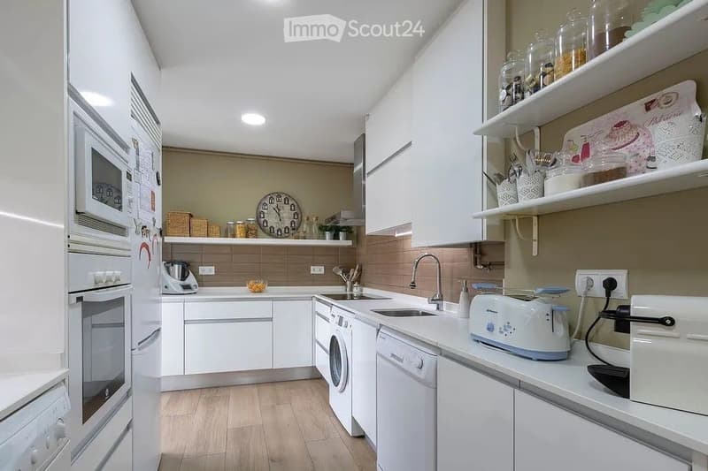 Modern kitchen with white cabinets, stainless steel appliances, and wooden flooring. Features include a refrigerator, oven, microwave, dishwasher, sink, faucet, toaster, clock, shelves, blender, and cupboard.