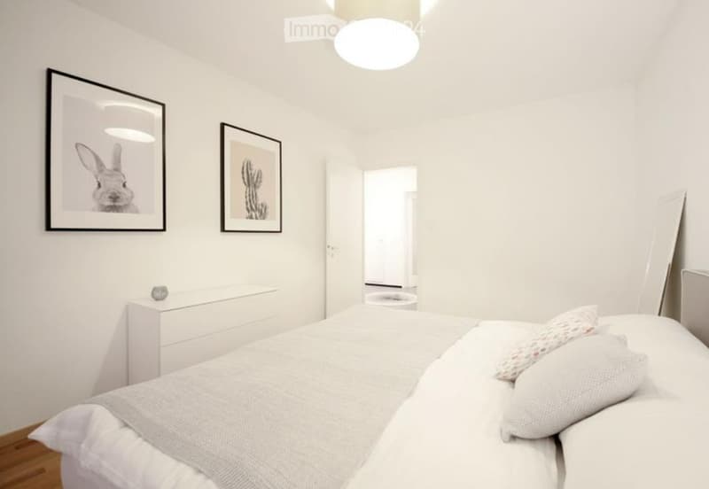 Modern, minimalist bedroom with white walls, a bed with white bedding, a nightstand, and framed artwork.