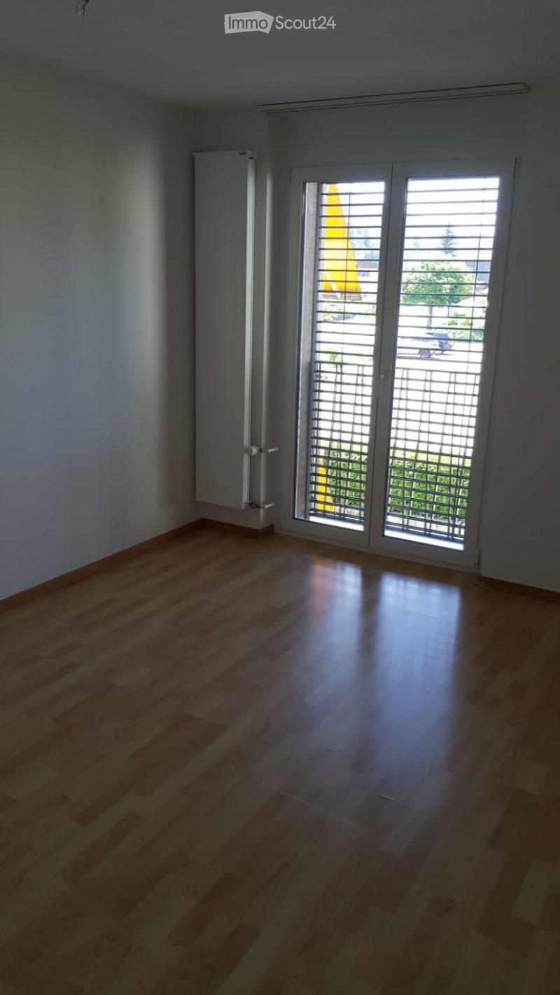 Empty room with wooden flooring, white walls, and large sliding glass doors leading to a balcony.