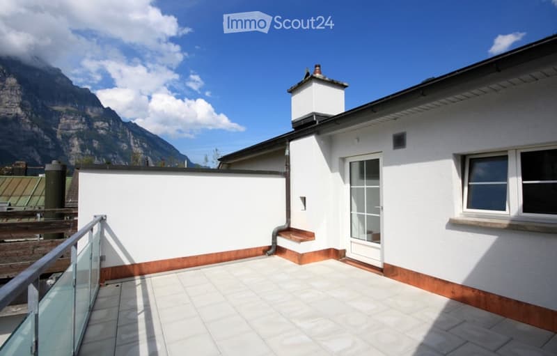 Balcony with white tiled floor, glass railing, and scenic mountain view in the background.