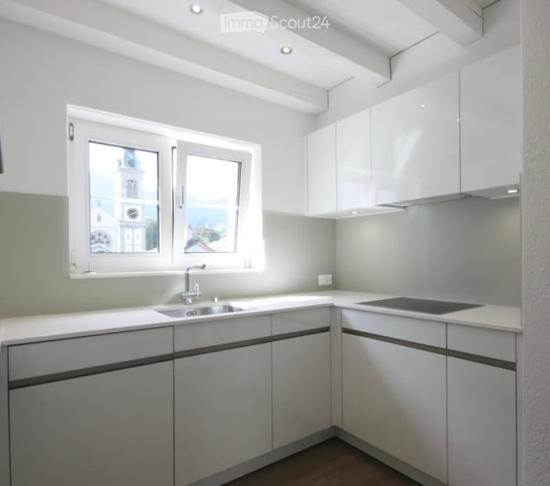 Modern kitchen with white cabinets, a sink, a stove, and large windows offering a view of a church tower.