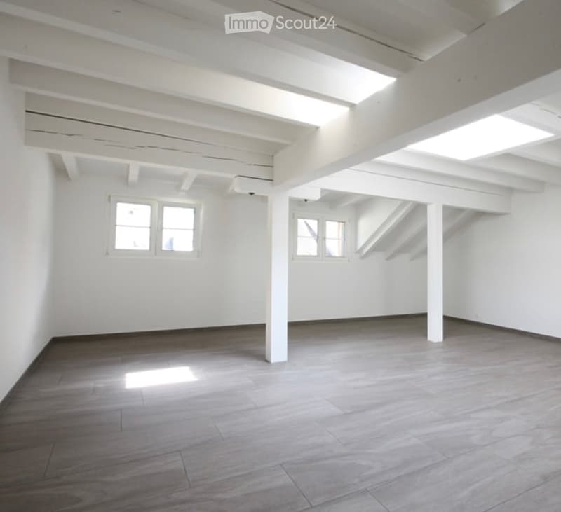 Completely empty room with white walls, wooden floor, and exposed white beams. No furniture or equipment.