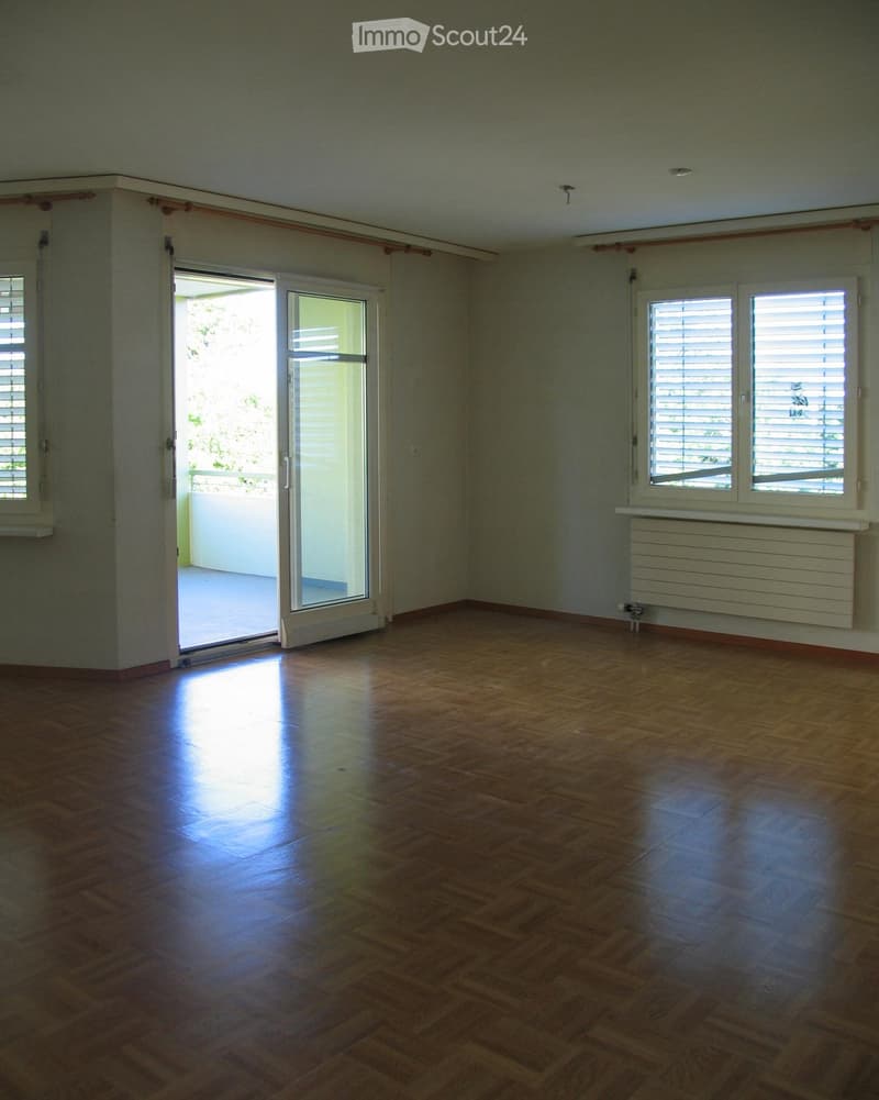 Empty room with wooden flooring, large windows, and a sliding glass door leading to a balcony.
