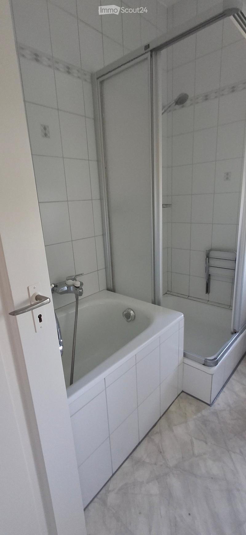 Modern bathroom with a white bathtub, a glass-enclosed shower stall, and a tiled floor.