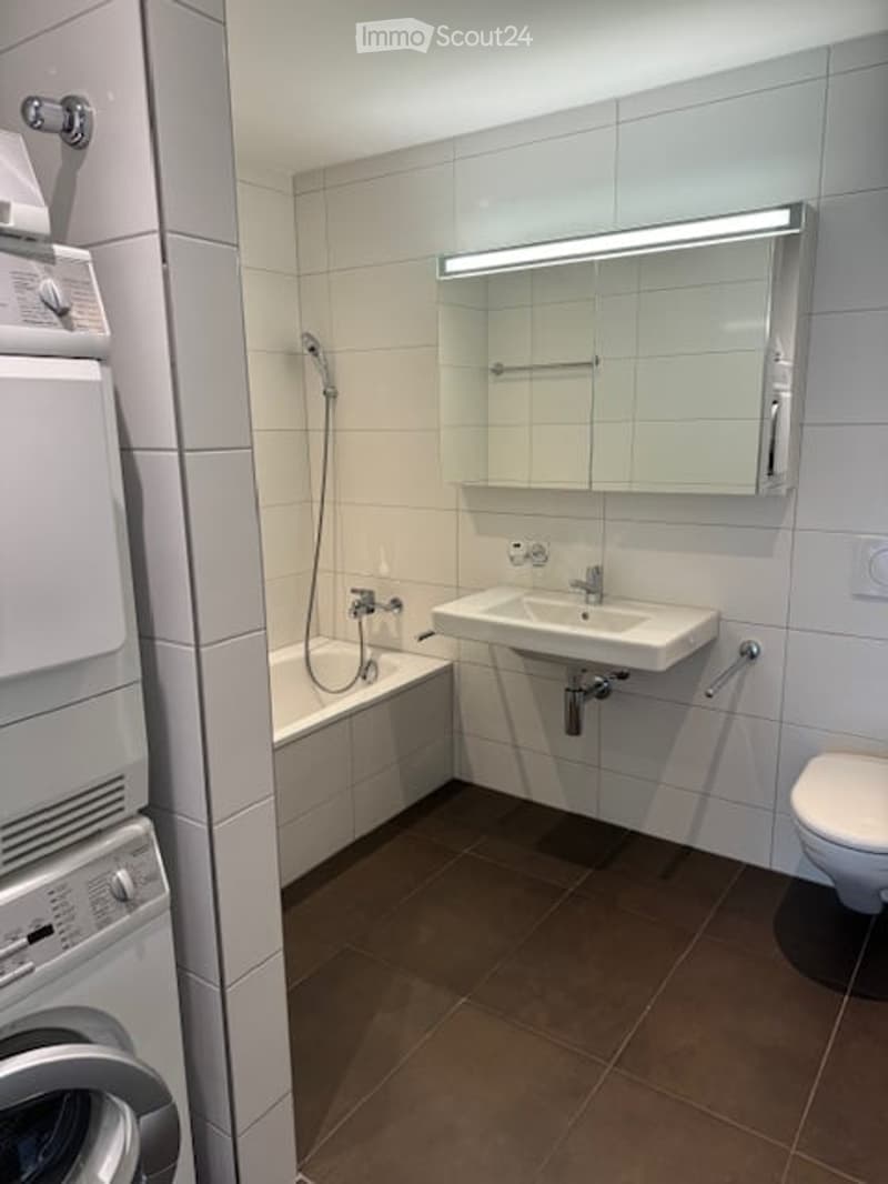 Modern bathroom with white tiles, a bathtub, a sink with a mirror, a toilet, and a washing machine.