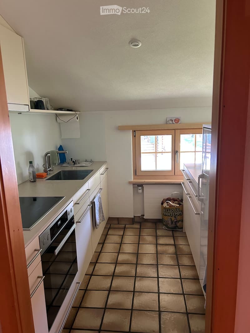 Compact kitchen with white cabinets, tiled floor, sink, oven, refrigerator, and a small window. Includes a trash bin and a towel on the counter.