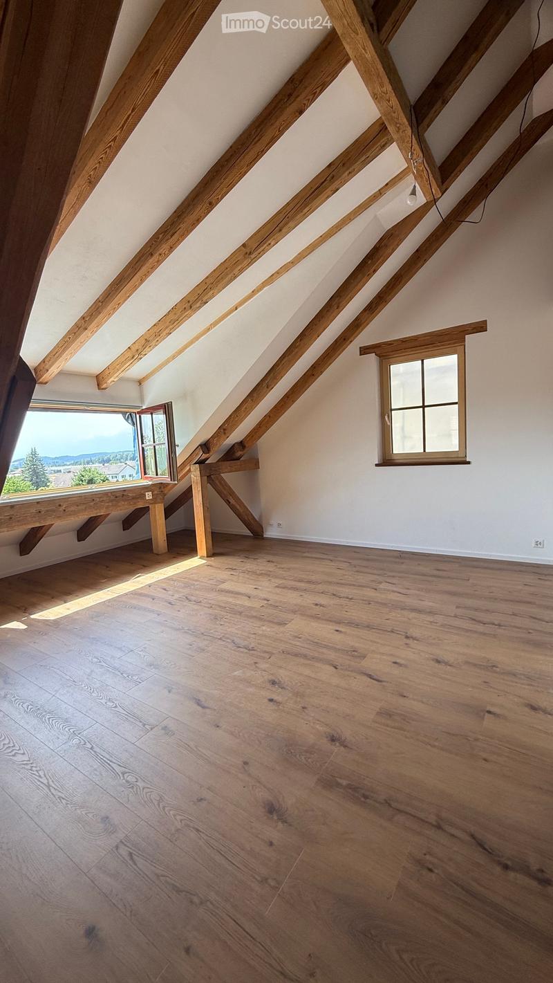 Empty attic space with wooden beams, wooden floor, and two windows offering natural light.