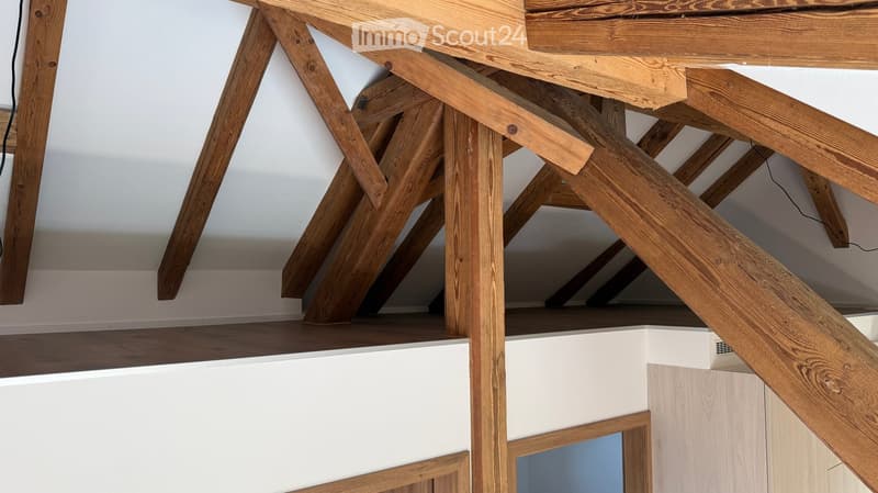 View of a wooden staircase with exposed beams and a white wall in the background.