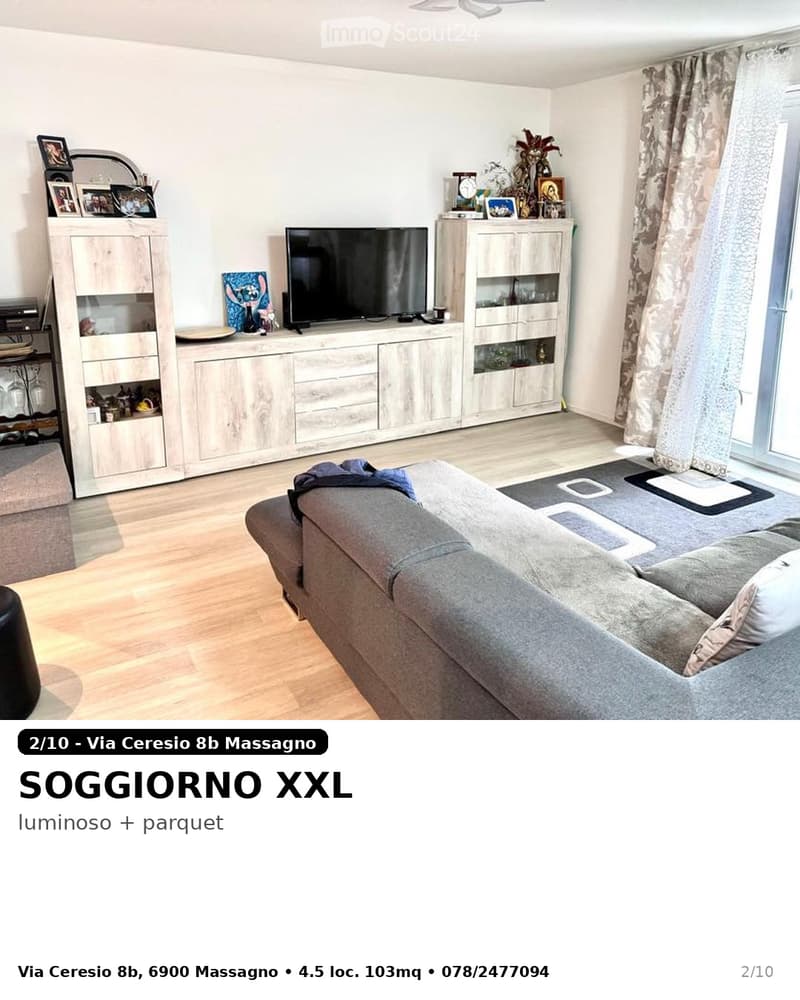 Bright living room with wooden flooring, large window with curtains, grey sectional sofa, coffee table, TV stand, and cabinets with glass doors.