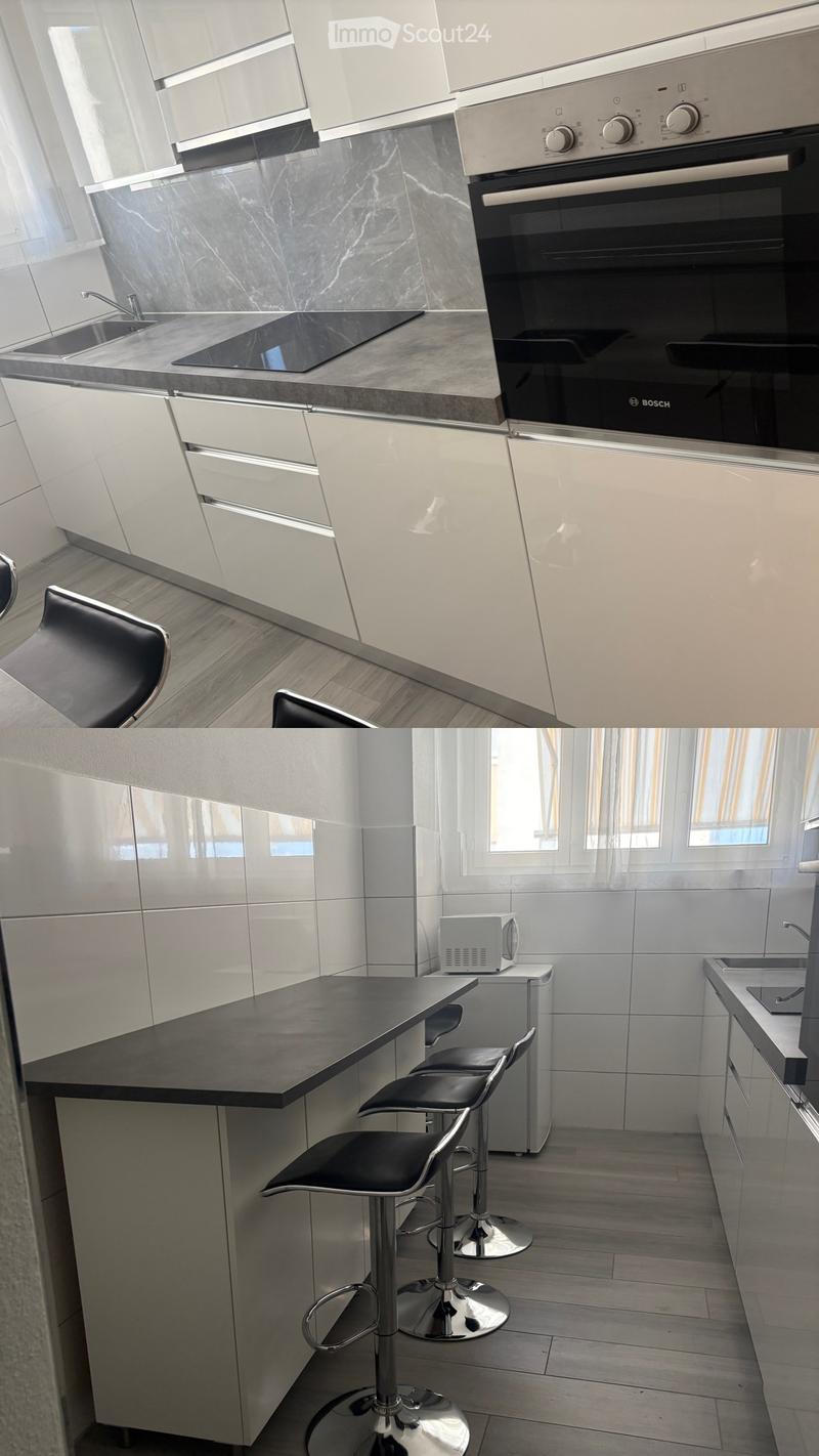 Modern kitchen with white cabinets, black countertops, stainless steel appliances, and three black bar stools.