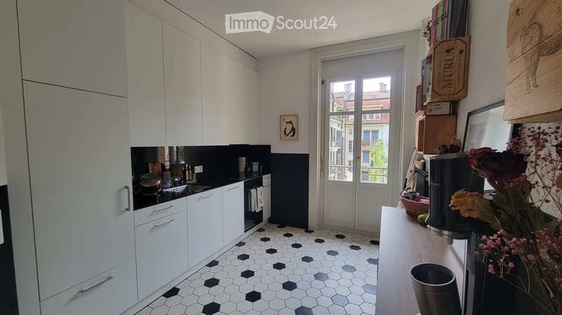 Modern kitchen with white cabinets, black countertop, hexagonal tile floor, and a windowed door leading outside.