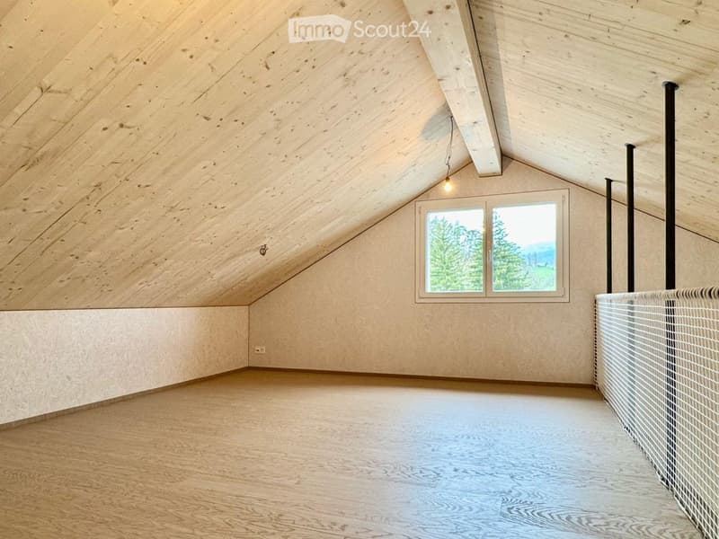 Empty attic space with wooden walls, ceiling, and floor, featuring a large window with a scenic view of trees and mountains.