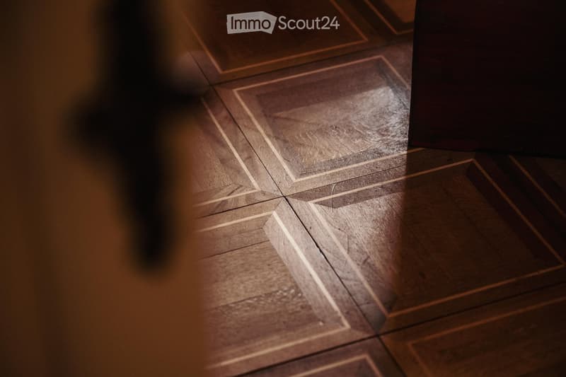 Close-up view of a wooden floor with a geometric pattern, showing light and shadow play on the surface.