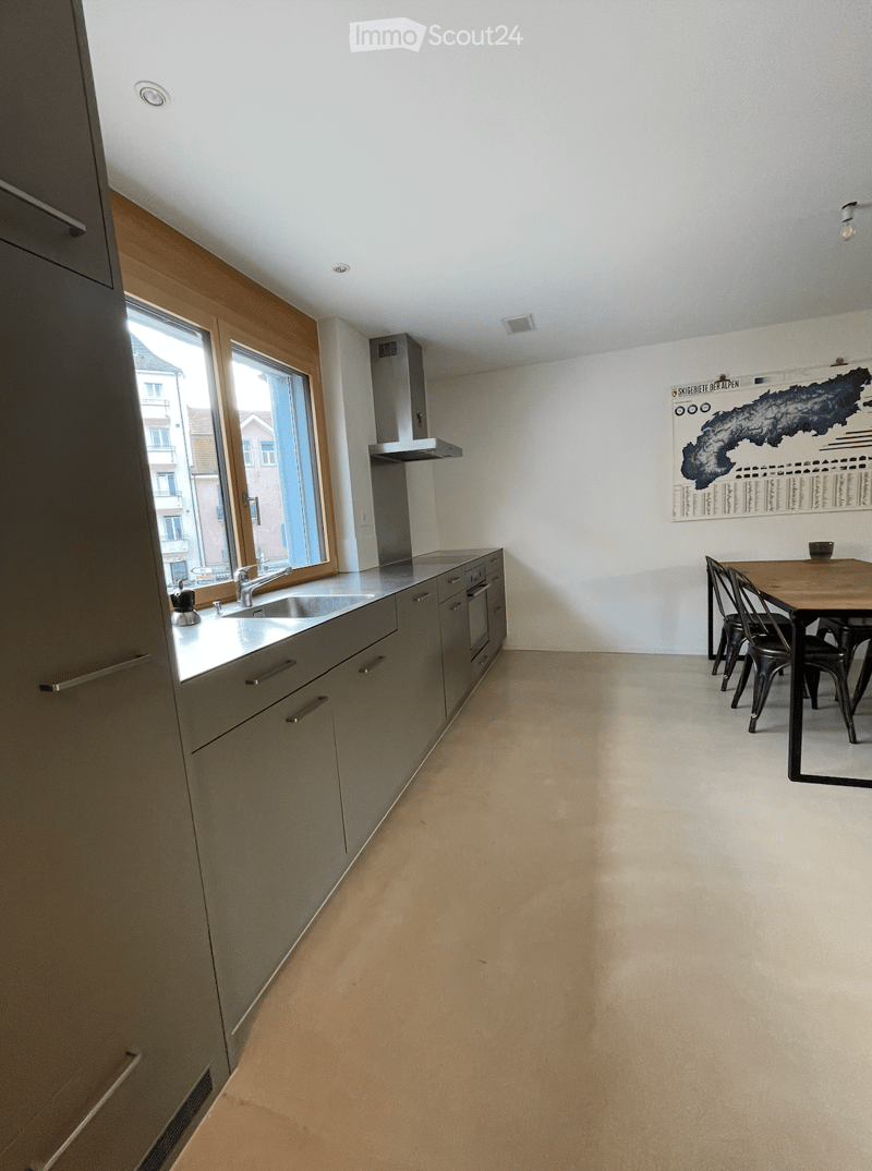 Modern kitchen with grey cabinets, a sink, and a small dining area with a table and chairs.